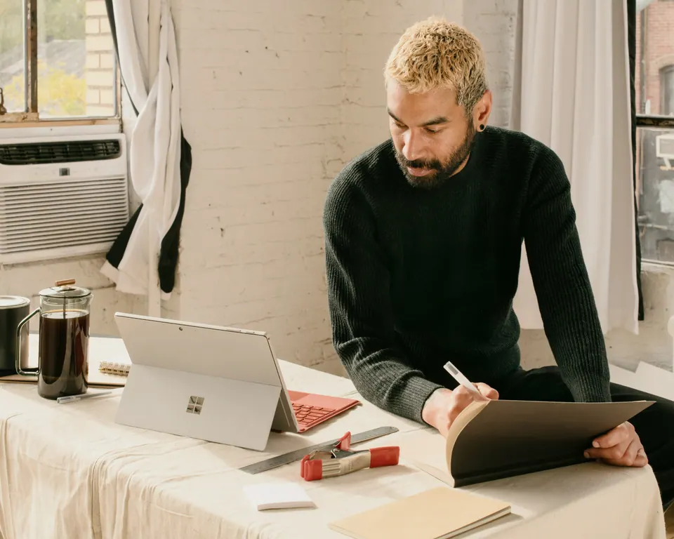 A person reviewing paperwork beside an open laptop.